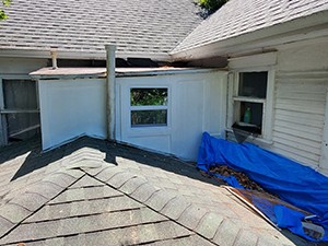 A section of a house with a flat roof, featuring windows, a blue tarp, and visible signs of wear and maintenance issues.